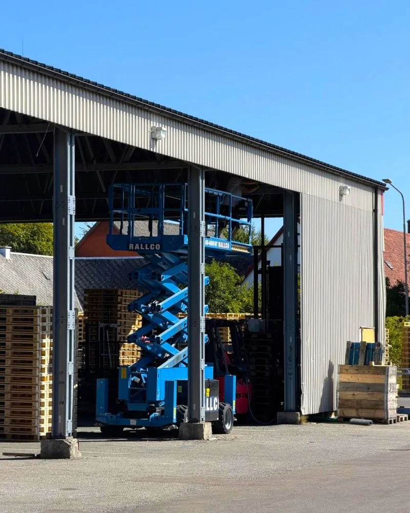 Blue scissor lift installing new bird-proofing at GLF's warehouse in Genarp for pallet protection.