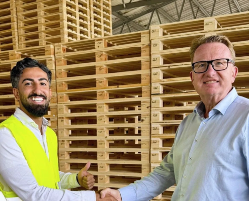 Taha Alnabeah skakar hand med en GLF-representant framför staplade träpallar i lagret i Genarp.