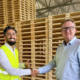 Taha Alnabeah shakes hands with a GLF representative in front of stacked wooden pallets at the warehouse in Genarp.