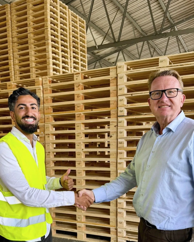Taha Alnabeah shaking hands in front of stacked wooden pallets for the KTP warehouse project.