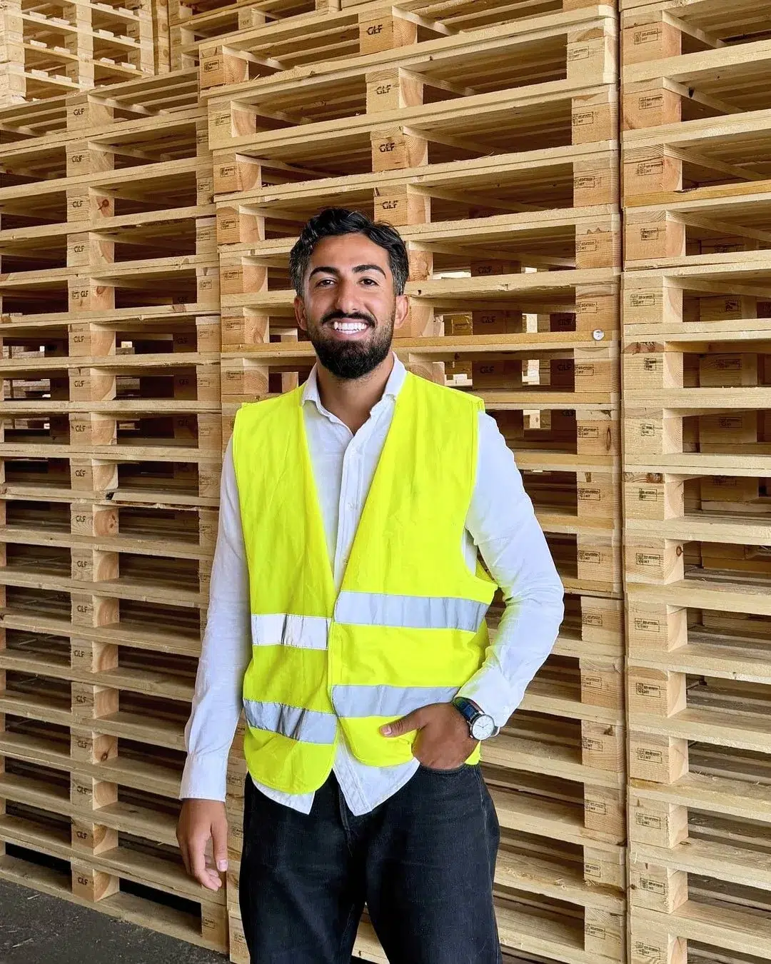 Taha Alnabeah wearing a high-visibility vest in front of stacked wooden pallets in GLF’s warehouse in Genarp.