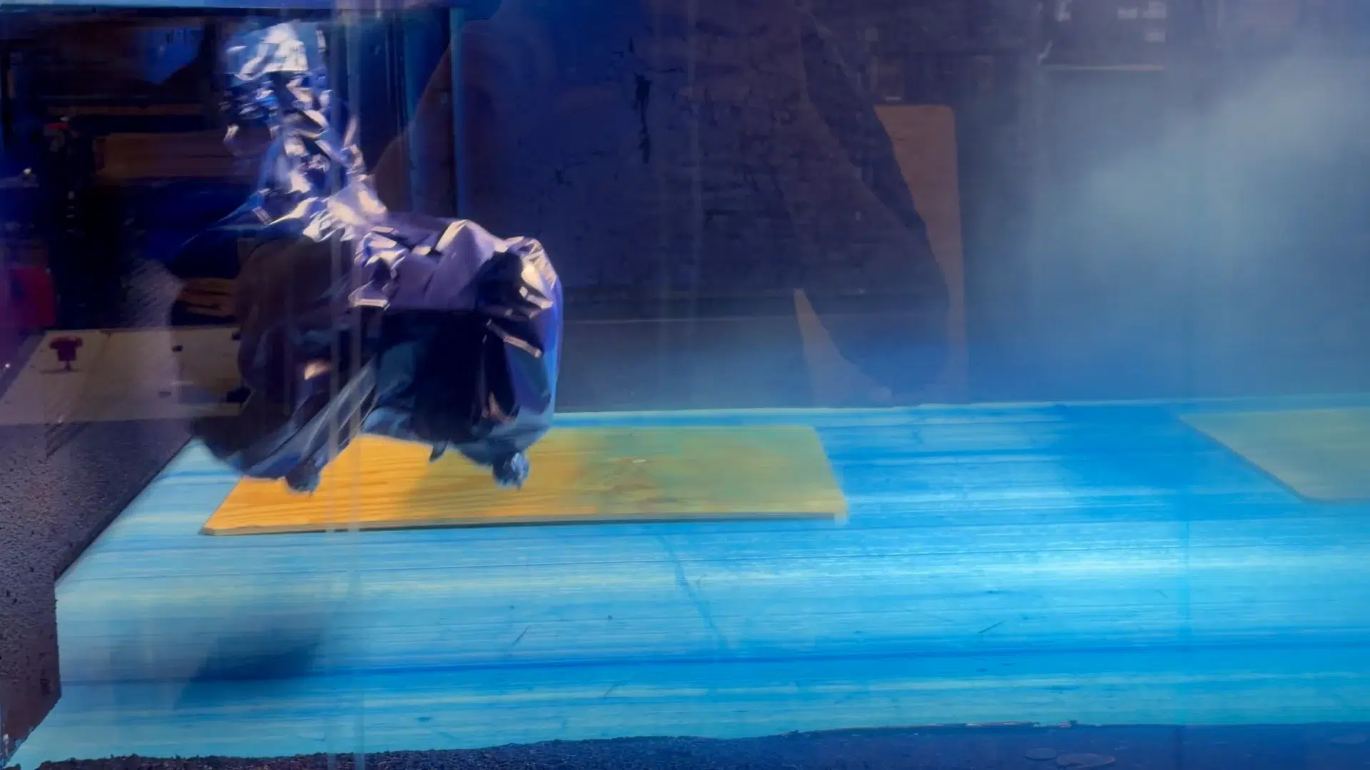 The painting equipment working over a plywood sheet behind the blue guards of the Böll-Tec machine.