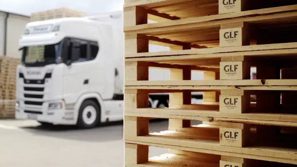 Stacked GLF wooden pallets in Genarp with a white delivery truck in the background.